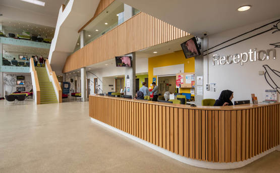 Reception area at a NHS site. The countertop is curved and has wooden panels. There's a 'Reception' sign above the space with the countertop and desks