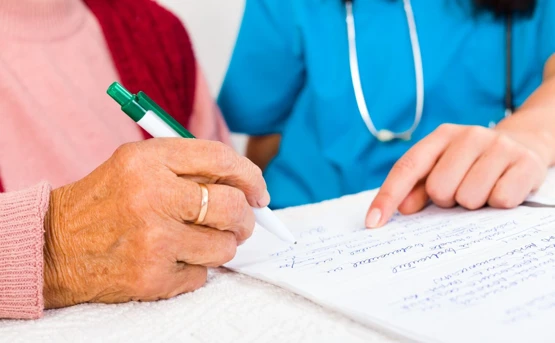 Elderly citizen filling out paperwork with the help of a healthcare professional