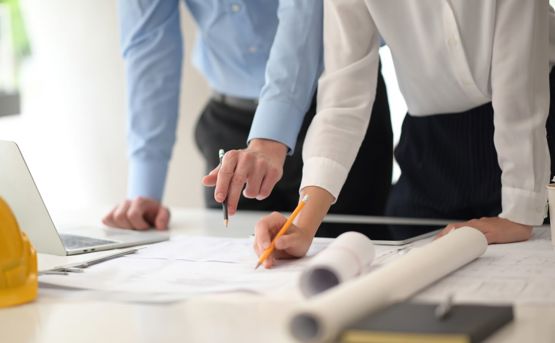 two people leaning over a desk looking at building plans