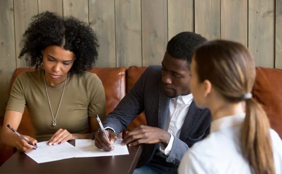 a couple signing paper on a table in front of a professional 