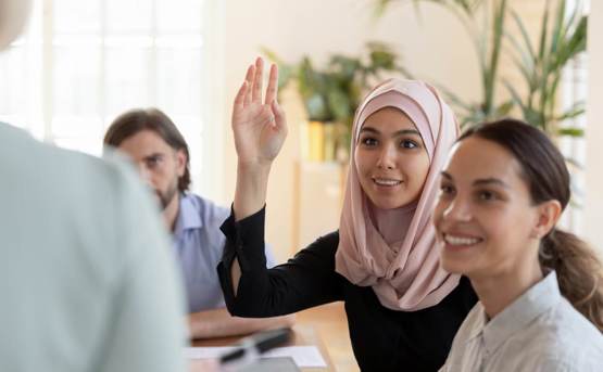 a group of people are watching someone present and a young woman puts her hand in the air