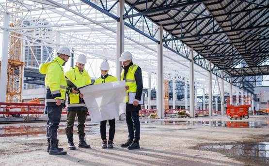 four construction workers in high-vis look at a large building plan