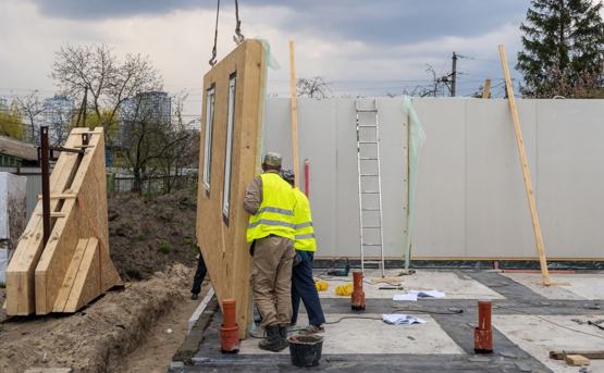 two construction workers in high vis lower a house frame into position