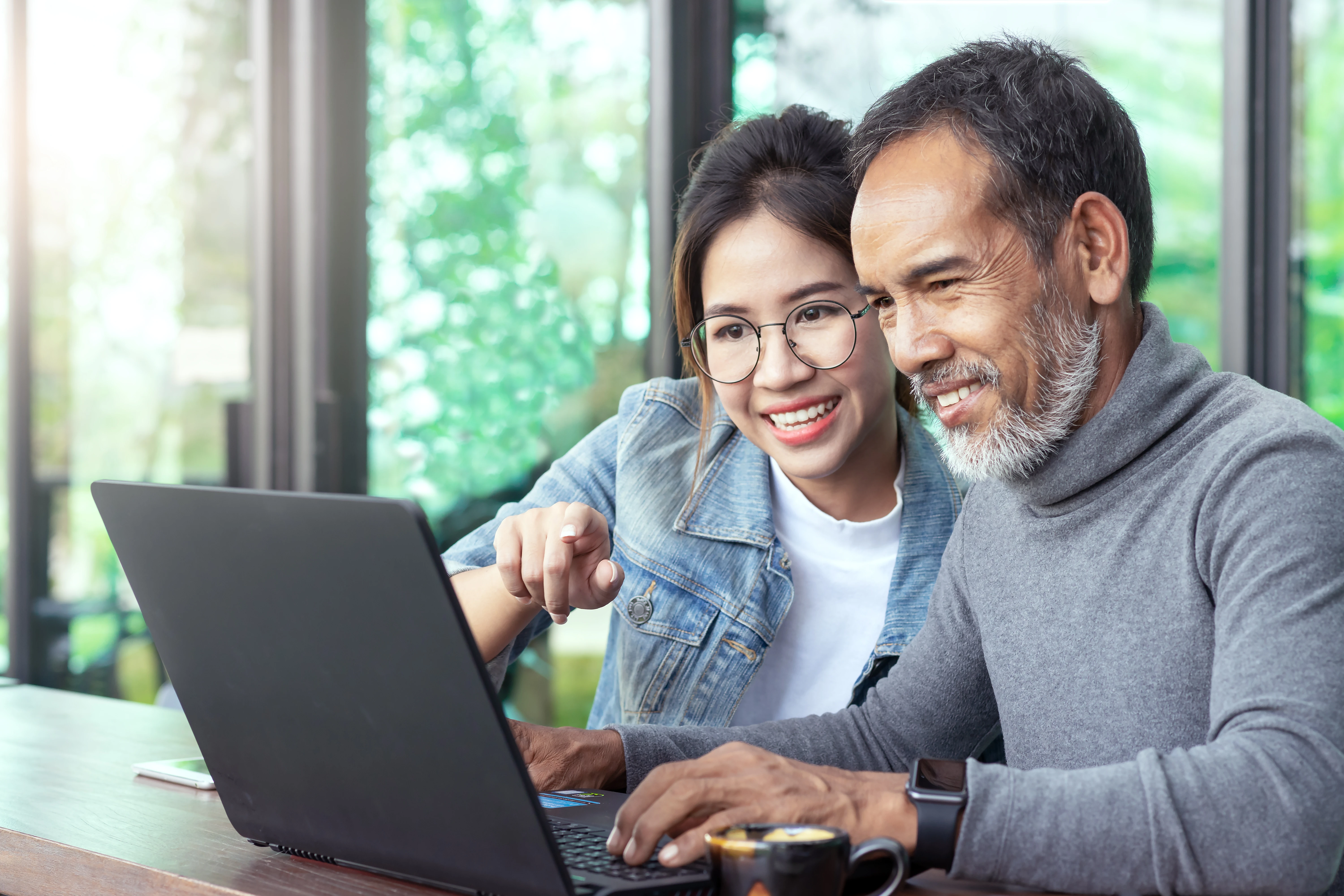 Stock image of Young Woman Teaching Older Man To Use Laptop