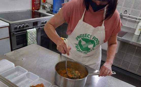 Woman with a Project Food apron on, making a stew and filling Tupperware 