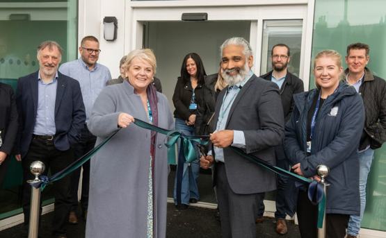 Eight people smiling as they're cutting a teal coloured ribbon